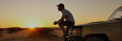 man watching the sunset on top of his car