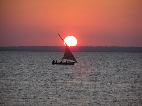 Dhow sailing through the ocean with the sunset behind it